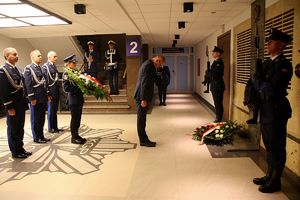 trzej oficerowie Policji i minister składają kwiaty przed tablicą pamięci. Po obu stronach tablicy stoją dwaj pełniący wartę honorową policjanci