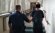zatrzymany mężczyzna zakuty w kajdanki z policjantem na korytarzu