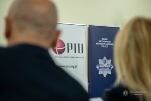 seminarium szkoleniowe, widoczny baner z napisem Polska Izba Ubezpieczeń, biuro Kryminalne Komendy Głównej Policji i zamazane głowy dwojga słuchaczy