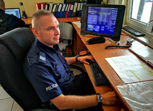 policjant dyżurny siedzi przy swoim stanowisku pracy, naprzeciwko stoi komputer