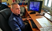 policjant dyżurny siedzi przy swoim stanowisku pracy, naprzeciwko stoi komputer