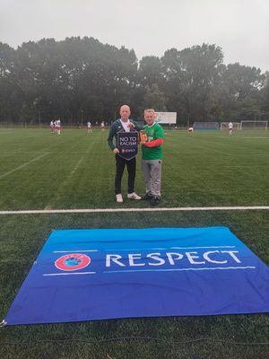 organizator meczu &quot;Nie dla rasizmu&quot; oraz selekcjoner Reprezentacji Polskiej Policji przekazują sobie pamiątki i stoją na na boisku tle baneru Respect