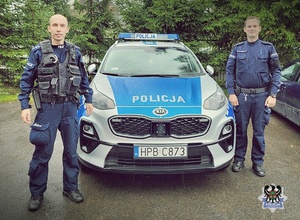 na zdjęciu umundurowani policjanci stoją obok radiowozu