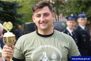 na zdjęciu st. asp. Piotr Zalewski w sportowym ubraniu, policjant w ręku trzyma puchar