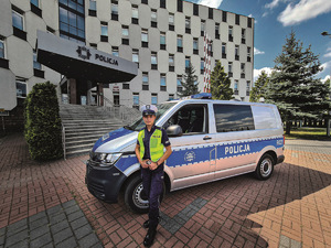 na zdjęciu policjant w kamizelce odblaskowej stoi obok zaparkowanego radiowozu marki volkswagen T6