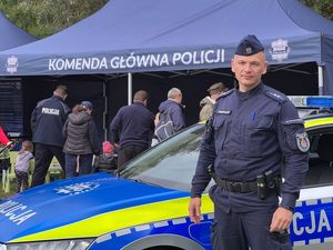 umundurowany policjant stoi przed radiowem i stoiskiem KGP na pikniku z okazji biegu Pamięci Rotmistrza Pileckiego