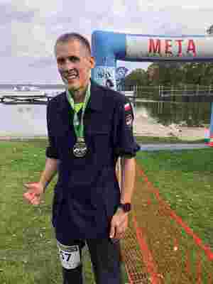 umundurowany mężczyzna pozuje do zdjęcia na mecie po zakończonym biegu przełajowym, na szyi nosi medal