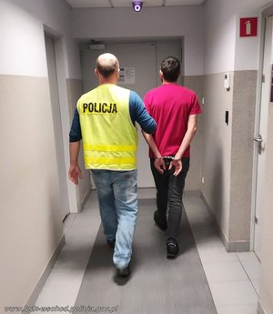 Policjant w żółtej kamizelce z napisem policja prowadzi zatrzymanego mężczyznę