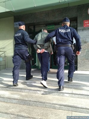 dwaj policjanci prowadzą zatrzymanego po schodach do sądu