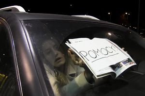 kobieta widoczna w tylnej szybie samochodu trzyma przy szybie auta kartkę: POMOCY