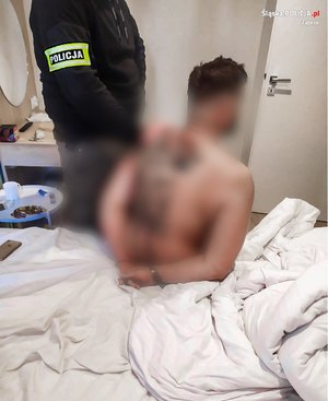 Policjant operacyjny z zatrzymanym mężczyzną, który ma nagi tors i siedzi na łóżku