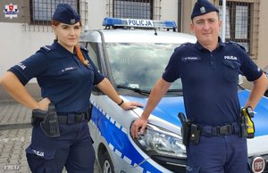 dwoje umundurowanych policjantów stoi przy radiowozie
