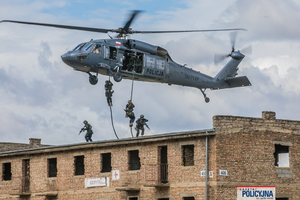 Policyjni kontrterroryści desantują się na linach z helikoptera na dach budynku.
