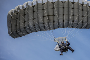Mężczyzna pod rozwiniętą czaszą spadochrony w trakcie lotu.