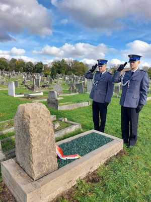 Dwaj oficerowie policji oddają honory przed nagrobkiem na cmentarzu.
