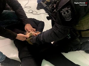 zatrzymany leży na podłodze, przy nim 2 policjantów zakłada kajdanki na ręce trzymane z tyłu