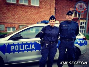 policjant i policjantka stoją przed radiowozem