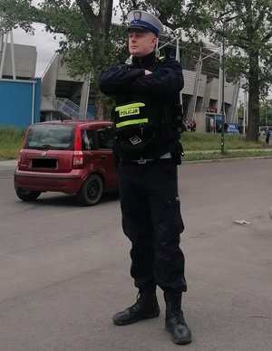 Umundurowany policjant ruchu drogowego podczas służby stoi w rejonie jezdni