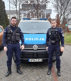 dwaj umundurowani policjanci stojący przy radiowozie