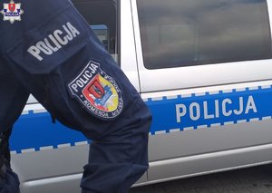 naszywka na rękawie policyjnego munduru z logiem Komendy Miejskiej Policji w Zamościu, w tle radiowóz