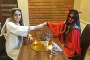 zdjęcie zrobione w pomieszczeniu przy stole siedzą osoby przebrane za diabła i anioła, podają sobie ręce nad stołem, zdjęcie kolorowe