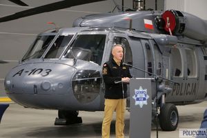 Komendant Główny Państwowej Straży Pożarnej przemawia na mównicy, w tle śmigłowiec typu S-70i Black Hawk