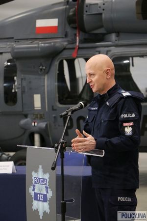 Komendant Główny Policji przemawia na mównicy, w tle stoi śmigłowiec typu S-70i Black Hawk