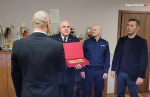 Zdjęcie Komendant straży w asyście policjanta i strażaka wręcza pamiątkę mężczyźnie