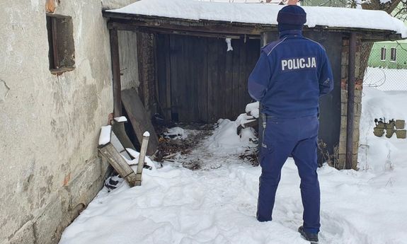 policjant podchodzi do prowizorycznej dobudówki, na ziemi leży śnieg