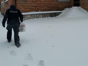 umundurowany policjant idzie w śniegu i niesie zakupy