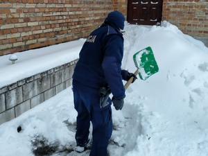 policjant odgarnia łopatą śnieg