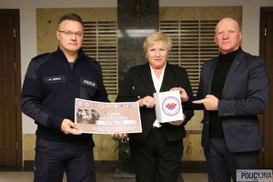 Szefowa Fundacji Pomocy Wdowom i Sierotom po Poległych Policjantach, przy niej stoją policjant z wypisanym czekiem i mężczyzna w garniturze