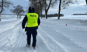 na zdjęciu policjant idący zasypaną śniegiem drogą, na drodze zaspy