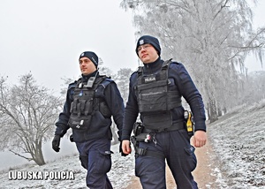 dwaj umundurowani policjanci w zimowej scenerii idą leśną drogą