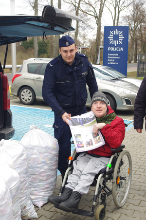 policjant wręcza mężczyźnie na wózku inwalidzkim prezent