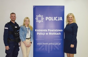 dwie kobiety i policjant stoją przy banerze promocyjnym Komendy powiatowej Policji w Mońkach
