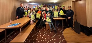 Policjanci pozują do zdjęcia z dziećmi i ich opiekunami. Dzieci trzymają w rękach gadżety profilaktyczne, które dostali od policjantów.
