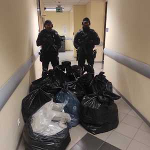 Na korytarzu budynku przed dwoma umundurowanymi policjantami z grupy realizacyjnej leżą zabezpieczone plastikowe worki wypełnione narkotykami