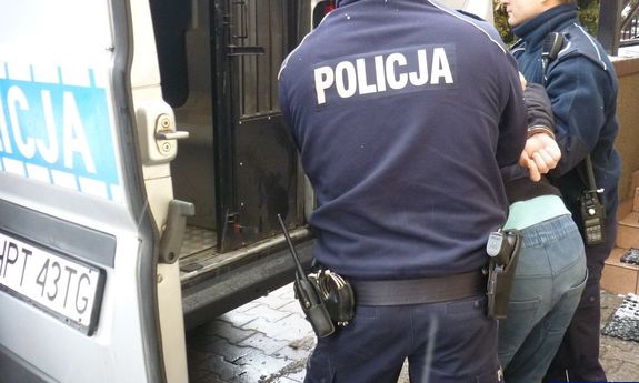 Zatrzymany mężczyzna prowadzony przez dwóch policjantów do radiowozu