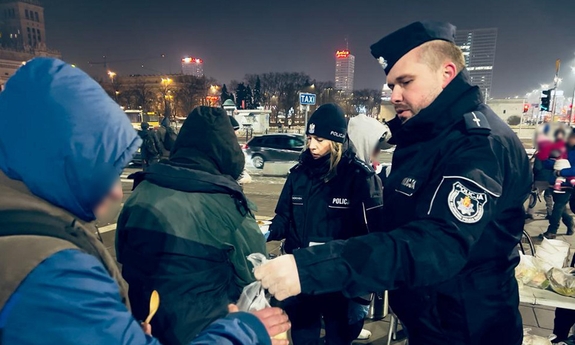 policjant i policjantka rozdają jedzenie potrzebującym