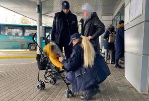 umundurowana policjantka kuca przed wózkiem z dzieckiem, obok stoi kobieta i umundurowany policjant