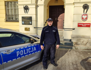 Policjant stoi przed budynkiem Komendy Stołecznej Policji obok radiowozu
