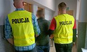 dwaj policjanci w żółtych kamizelkach z napisem Policja prowadzą zatrzymanego