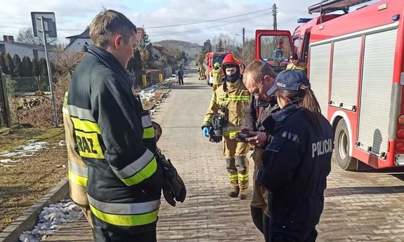 na zdjęciu policjantka rozmawia ze strażakami, w tle woź strażacki