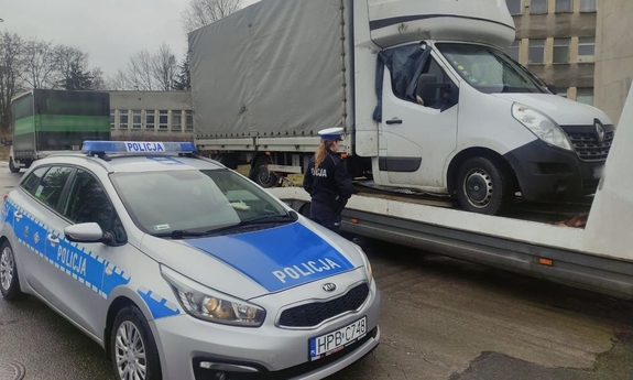 oznakowany radiowóz, policjantka stoi obok lawety, na której znajduje się samochód typu bus