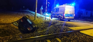 Zdjęcie przedstawia samochód, który dachował w rejonie przejazdu kolejowego, w tle radiowóz Policji