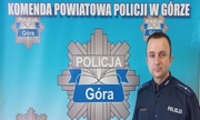 policjant w mundurze na tle niebieskiej planszy z napisem Komenda Powiatowa Policji w Górze oraz gwiazdą policyjną