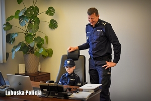 umundurowany policjant stoi obok chłopca, który siedzi przy biurku