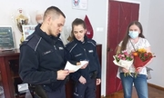 policjant wraz z policjantką czytają podziękowania. Obok stoi mama dziewczynki wraz z bukietem kwiatów, której córeczka te podziękowania napisała
