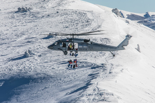 Ratownicy górscy desantują się wraz ze sprzętem na stoku góry z policyjnego śmigłowca.